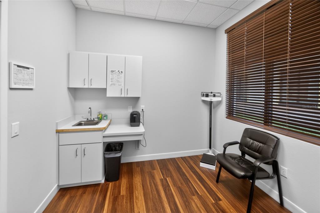 A medical exam room features white cabinets, a sink, a scale, and a black chair — 4064 E STATE ROAD 44, WILDWOOD, FL