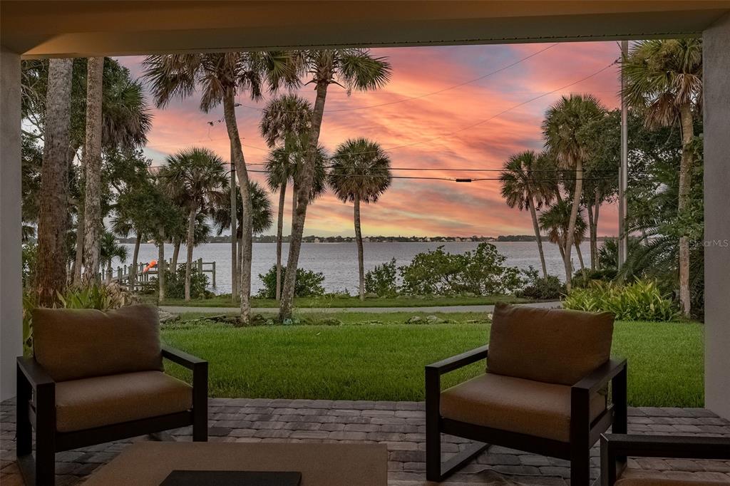 A covered patio with two chairs overlooks a grassy lawn, palm trees, and a lake — 11 BAYSHORE COURT, ROCKLEDGE, FL