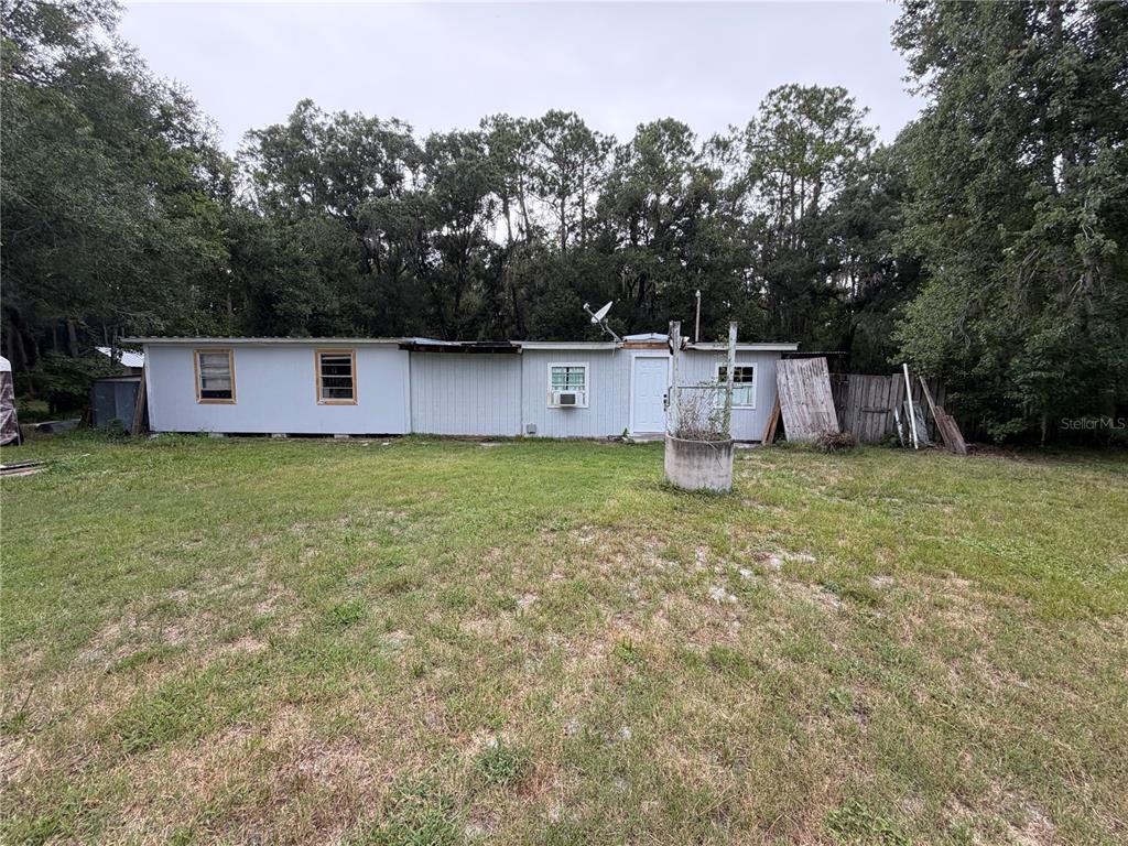 A single-story mobile home with light gray siding sits on a grassy lot near trees — 6900 ANGUS VALLEY DRIVE, WESLEY CHAPEL, FL