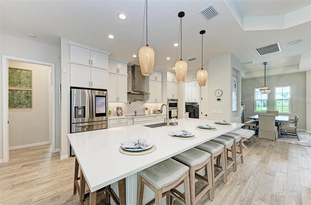 A modern kitchen features a large white quartz island, pendant lighting, and stainless steel appliances — 8211 37TH AVENUE CIRCLE W, BRADENTON, FL