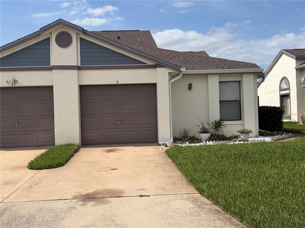 A beige duplex house features brown garage doors, a concrete driveway, and a small garden — 31 LAKEPOINTE CIRCLE, KISSIMMEE, FL
