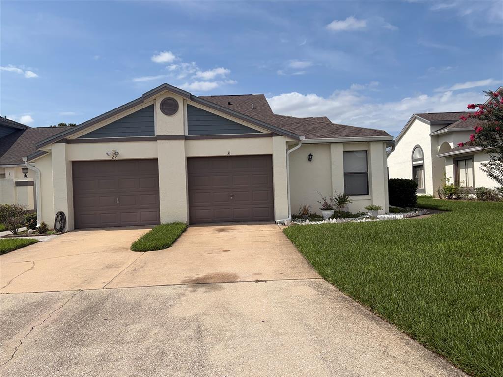 A duplex house features two brown garage doors, a beige stucco exterior, and a lawn — 31 LAKEPOINTE CIRCLE, KISSIMMEE, FL