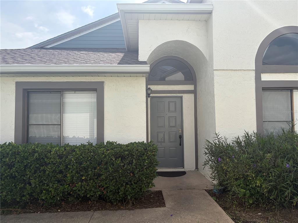 The exterior of a house features a gray front door, arched windows, and green landscaping — 31 LAKEPOINTE CIRCLE, KISSIMMEE, FL