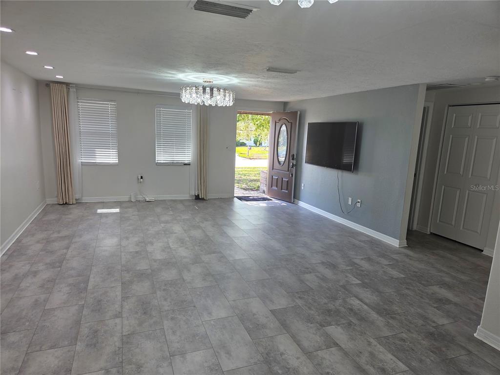 A living room features gray tile flooring, a mounted television, and a crystal chandelier — 3922 COCHISE TER,, SARASOTA, FL