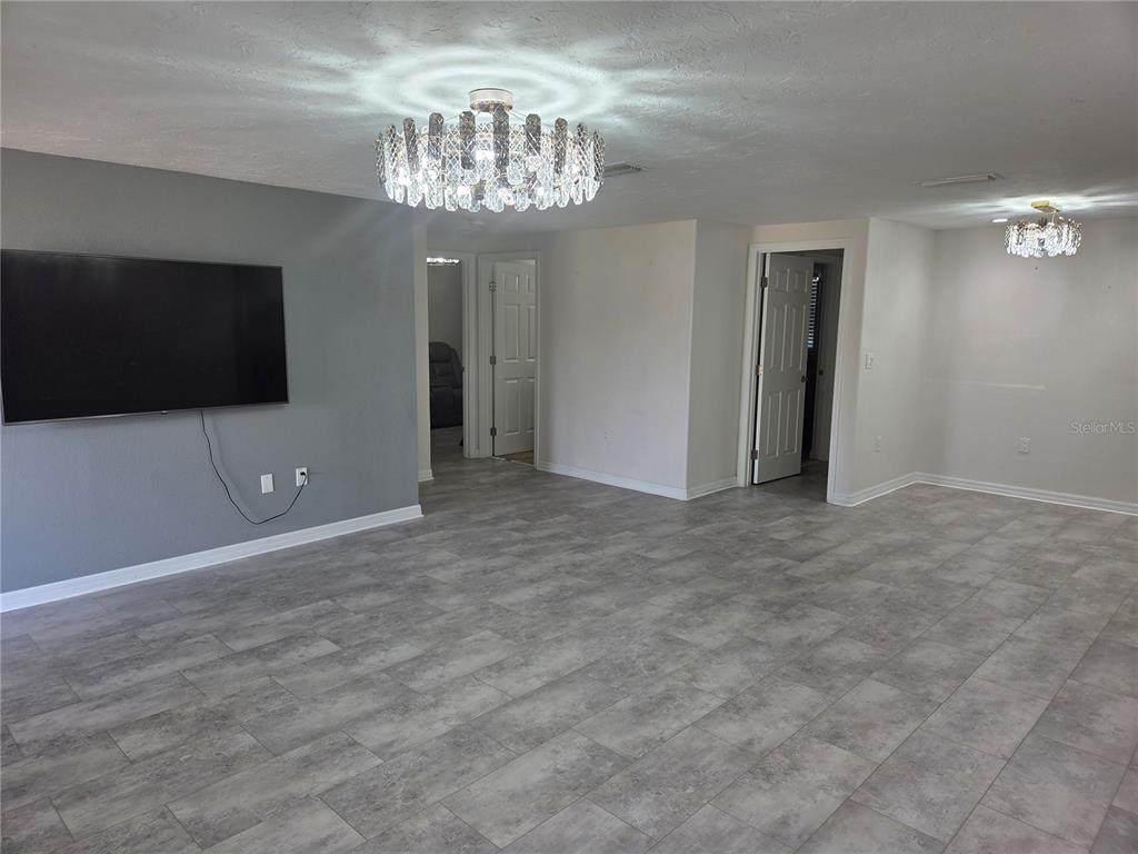 A living room features gray tile flooring, a wall-mounted television, and two crystal chandeliers — 3922 COCHISE TER,, SARASOTA, FL