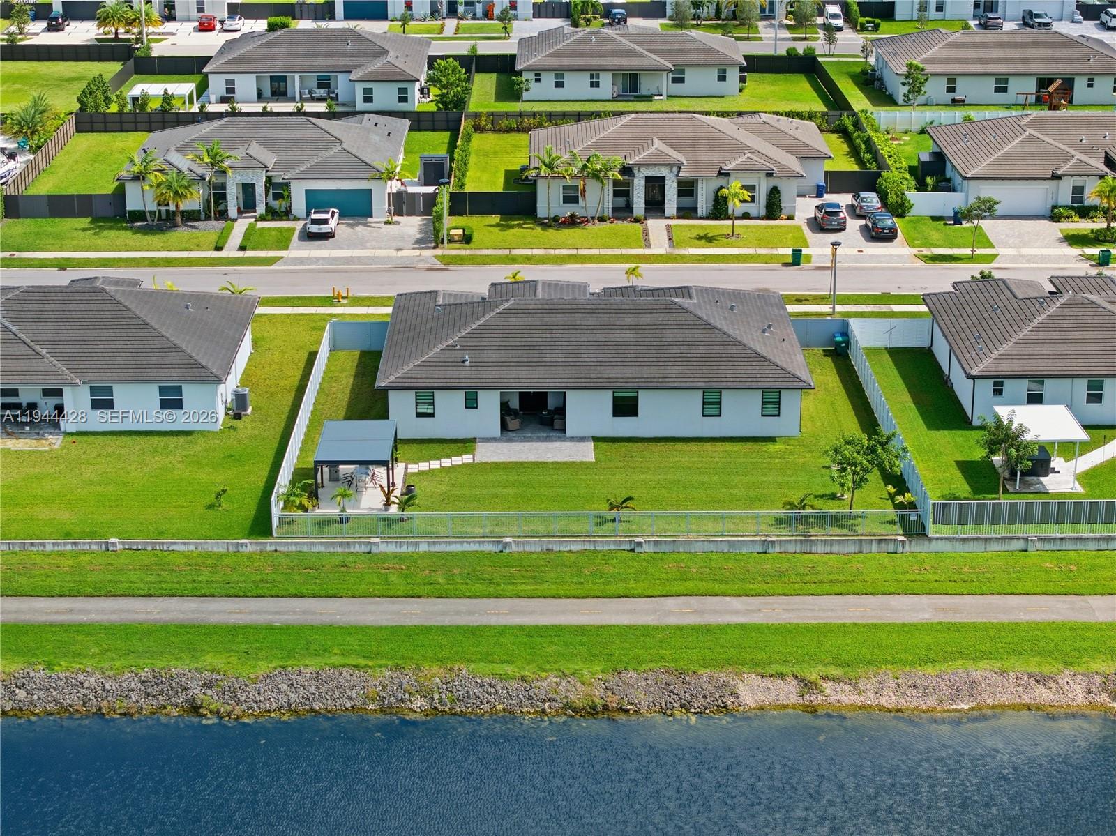 An aerial view shows a residential neighborhood with houses, fenced backyards, and a waterfront path — 19080 SW 133RD CT, Miami FL 33177, MIAMI, FL