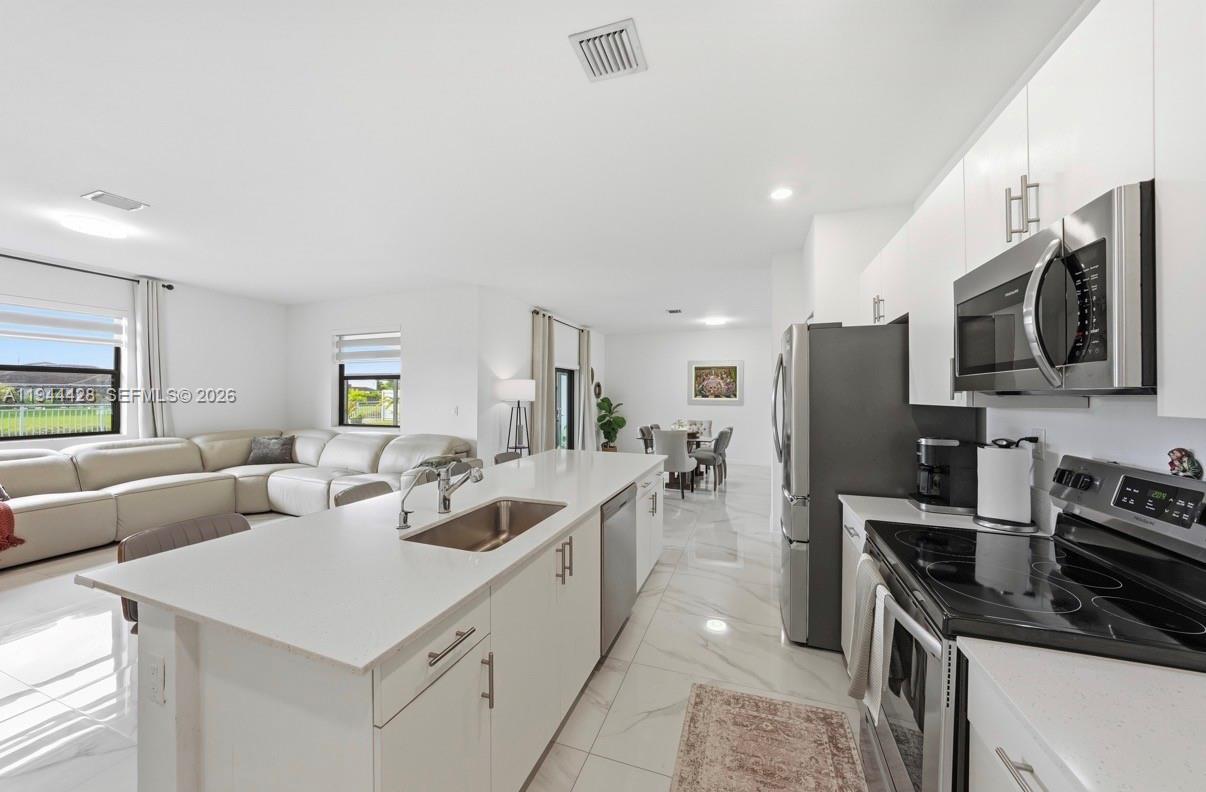 A modern kitchen with white cabinets and quartz countertops opens into a living area — 19080 SW 133RD CT, Miami FL 33177, MIAMI, FL