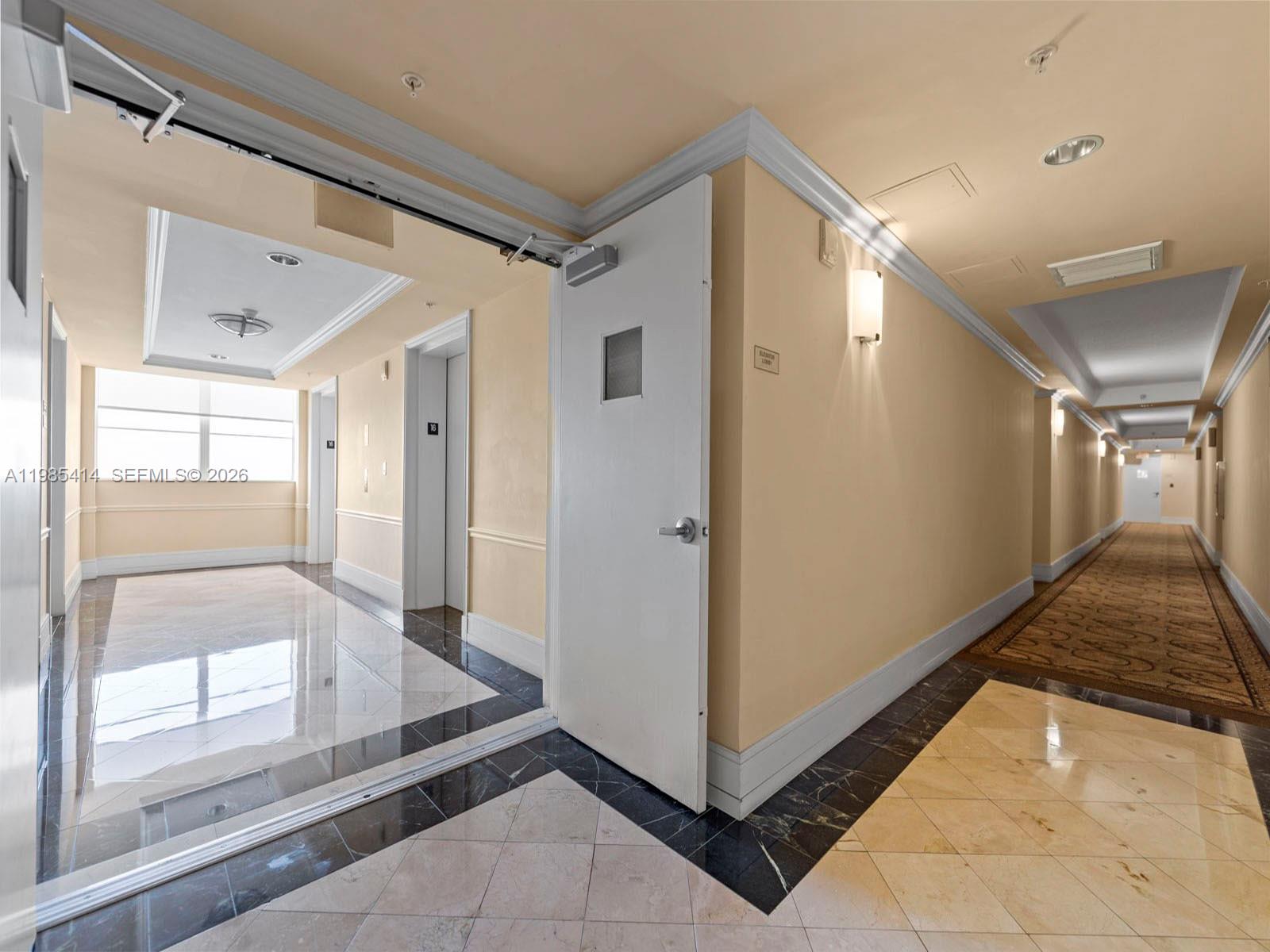A hallway with a white door, marble flooring, and a carpeted corridor leading to elevators — 3232 SW 22nd Ter # 1609, Miami FL 33145, MIAMI, FL