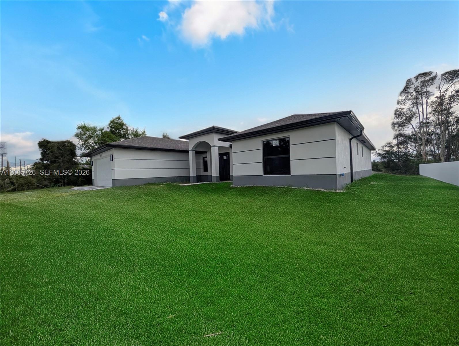 A modern, single-story house with a white stucco exterior and a large green lawn — 813 Bell Blvd S, Lehigh Acres FL 33974, LEHIGH ACRES, FL