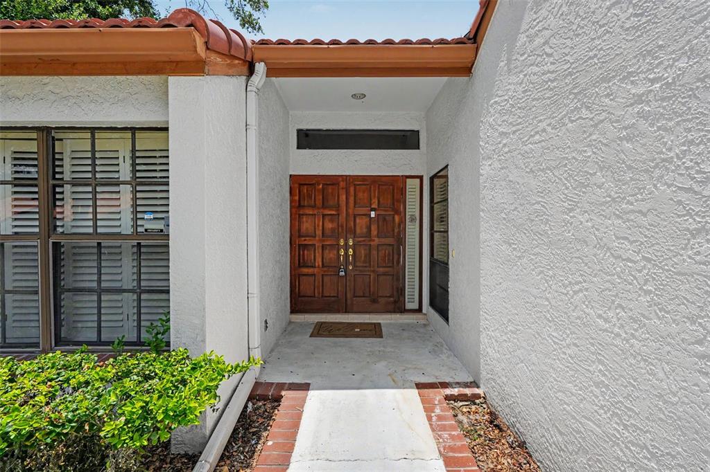 A concrete walkway leads to a recessed entryway with double wooden doors and stucco walls — 11502 ROBLES DEL RIO PLACE, TEMPLE TERRACE, FL