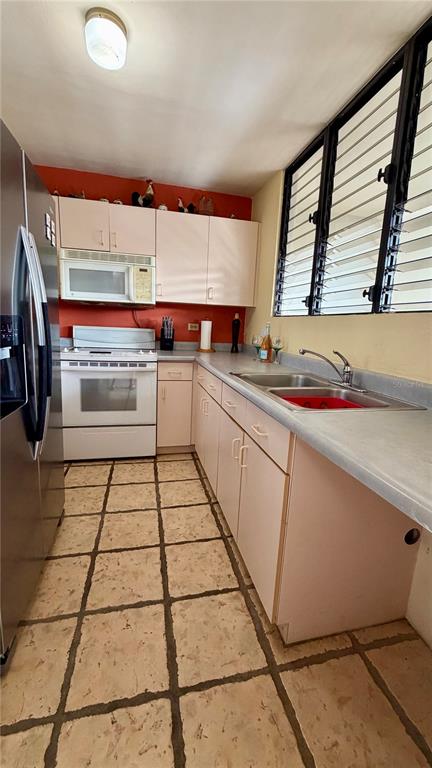 A kitchen with light-colored cabinets, a white stove, a stainless steel sink, and tiled floors — CARR 3 KM 66.7 CALA DE HUCARES UNIT C210, NAGUABO, PR