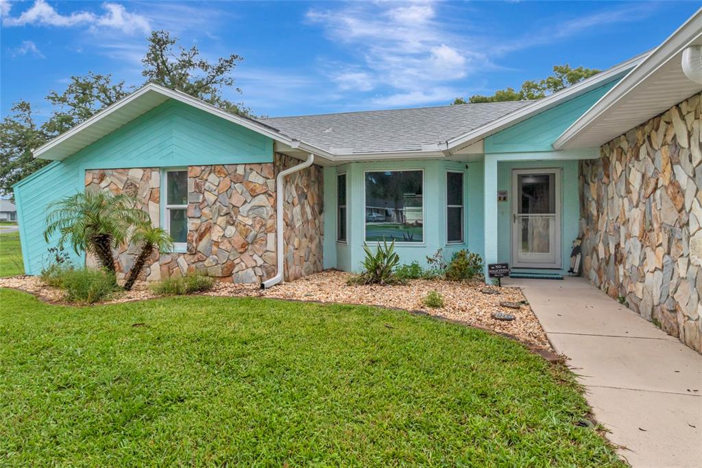 A single-story house with light blue siding, stone veneer accents, and a front walkway — 5325 ABAGAIL DRIVE, SPRING HILL, FL