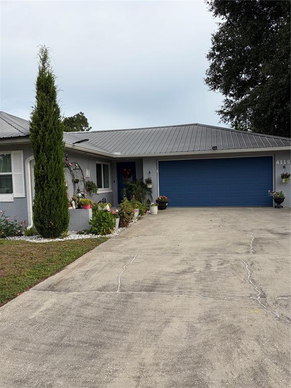 A single-story house with a gray exterior, metal roof, blue garage door, and concrete driveway — 4119 SUNNY LAND DRIVE, LAKELAND, FL