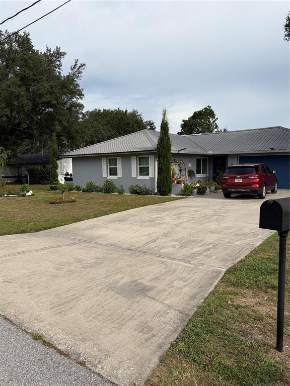 A gray single-story house with a metal roof features a concrete driveway and red SUV — 4119 SUNNY LAND DRIVE, LAKELAND, FL