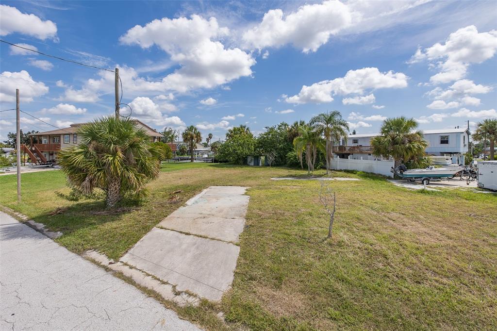 A vacant grassy lot features a concrete driveway pad and several palm trees under blue skies — 13008 BALLAST COURT, HUDSON, FL