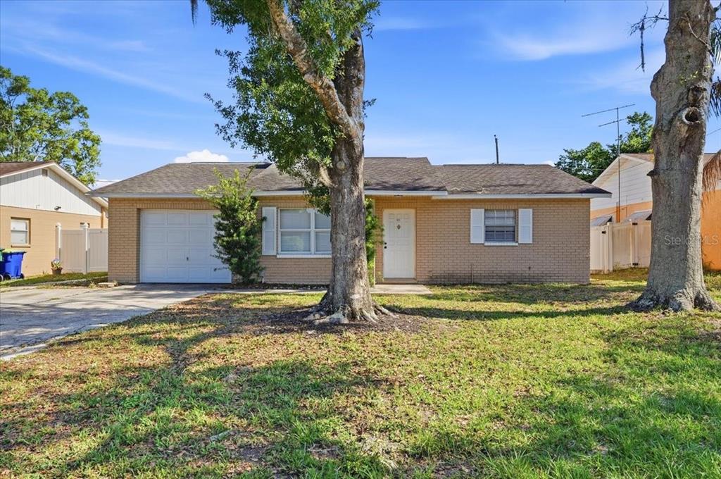A single-story brick house with a garage, a front door, and two large trees — 4624 WISTERIA DRIVE, ZEPHYRHILLS, FL