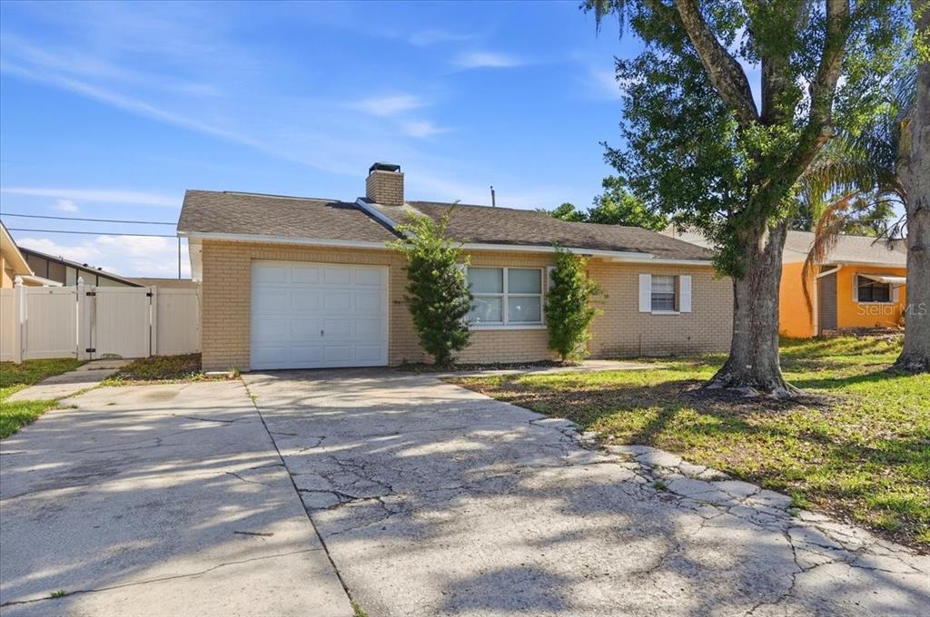 A single-story brick house with a garage, a chimney, and a cracked concrete driveway — 4624 WISTERIA DRIVE, ZEPHYRHILLS, FL