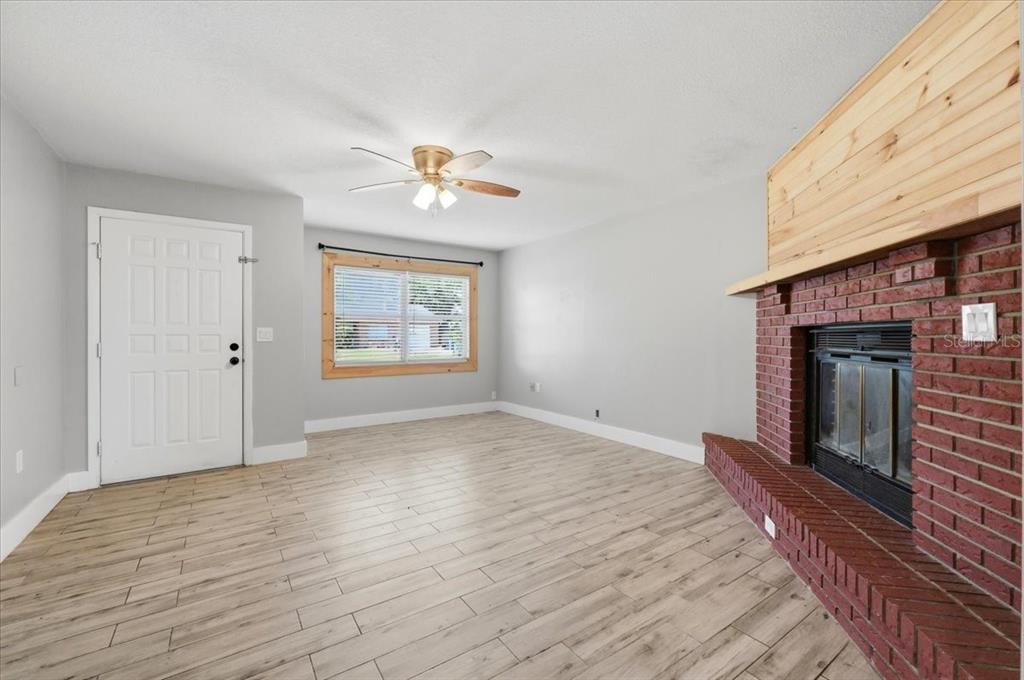A living room features light wood-look tile flooring, a brick fireplace, and a ceiling fan — 4624 WISTERIA DRIVE, ZEPHYRHILLS, FL