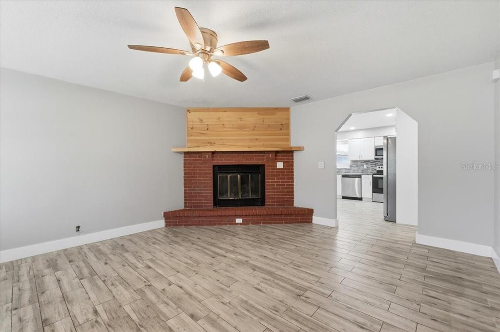 A living room features a corner brick fireplace with a wood mantel and tile flooring — 4624 WISTERIA DRIVE, ZEPHYRHILLS, FL