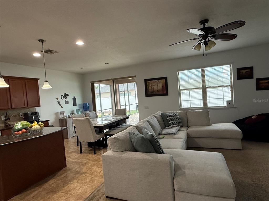 An open-concept living and dining area features a sectional sofa, kitchen island, and sliding doors — 759 SUGAR CAMP WAY, BROOKSVILLE, FL