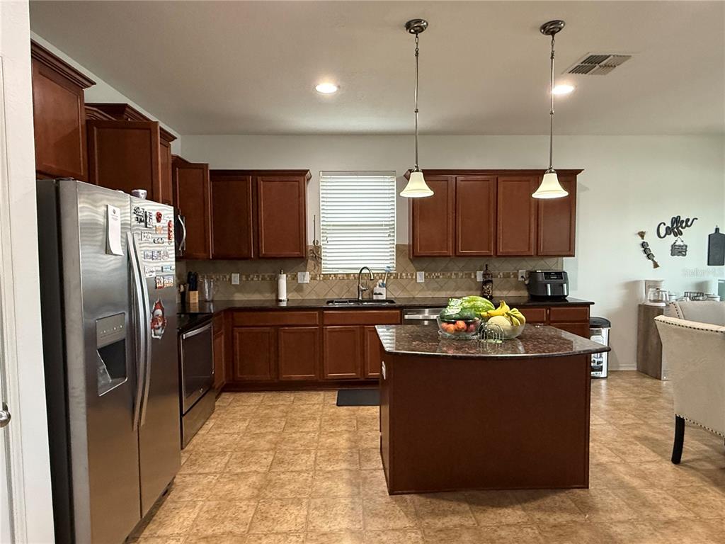 A kitchen features dark wood cabinets, granite countertops, a center island, and stainless steel appliances — 759 SUGAR CAMP WAY, BROOKSVILLE, FL