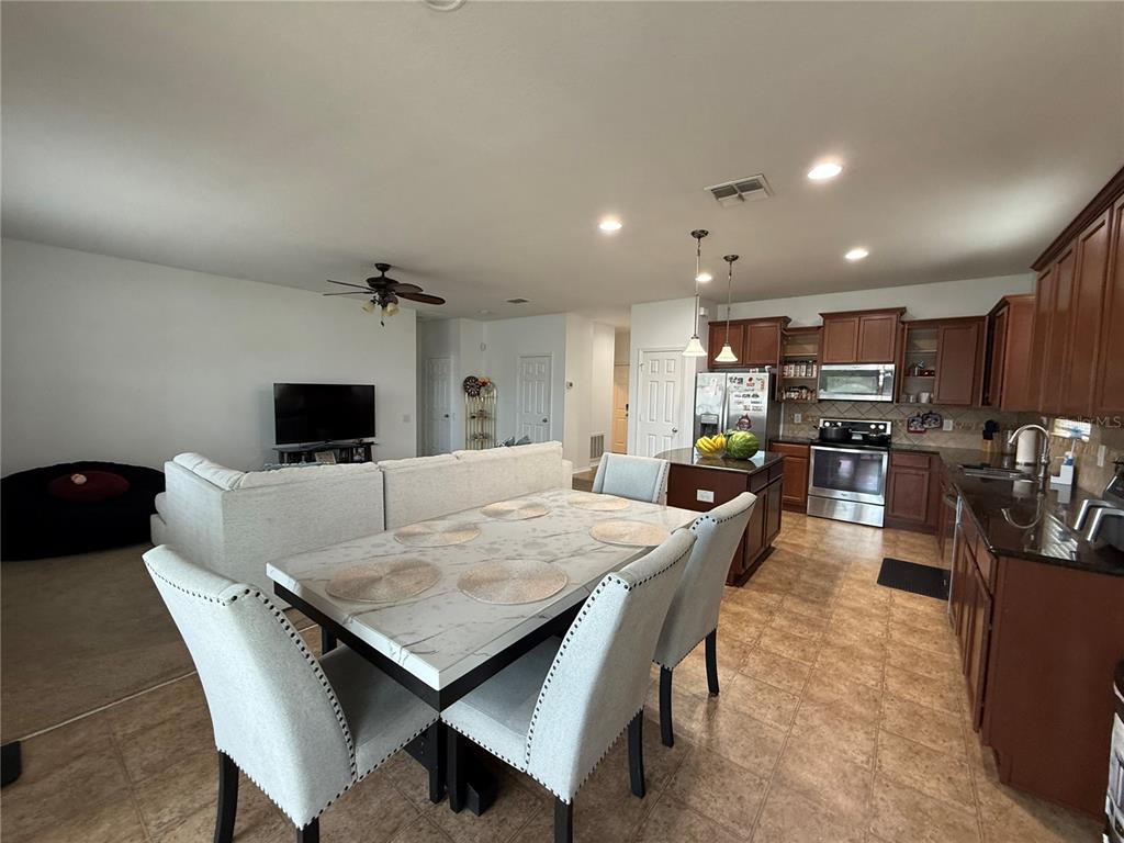 An open-concept kitchen and dining area features dark wood cabinets, granite countertops, and tile flooring — 759 SUGAR CAMP WAY, BROOKSVILLE, FL