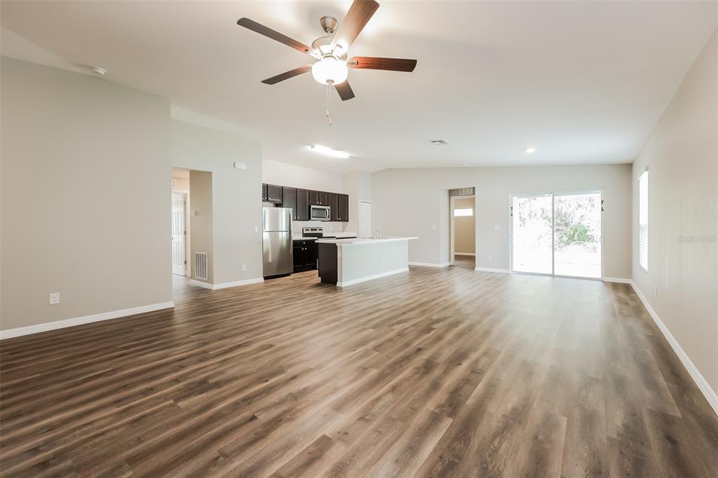 An open-concept living area features wood-look flooring, a ceiling fan, and a kitchen with dark cabinets — 3673 SHALIMAR TERRACE, NORTH PORT, FL