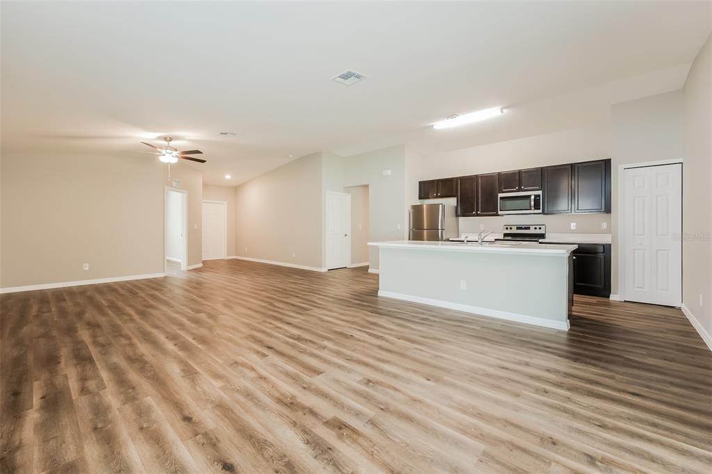 An open-concept living area features wood-look flooring, a kitchen with dark cabinets, and a breakfast bar — 3673 SHALIMAR TERRACE, NORTH PORT, FL