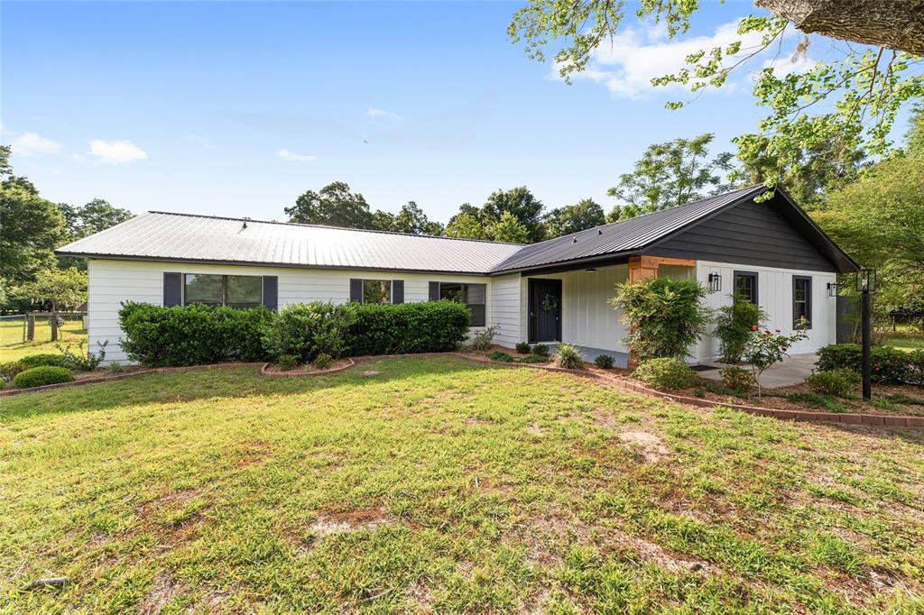 A single-story house with white vertical siding, a dark metal roof, and a concrete driveway — 10575 SW 27TH AVENUE, OCALA, FL