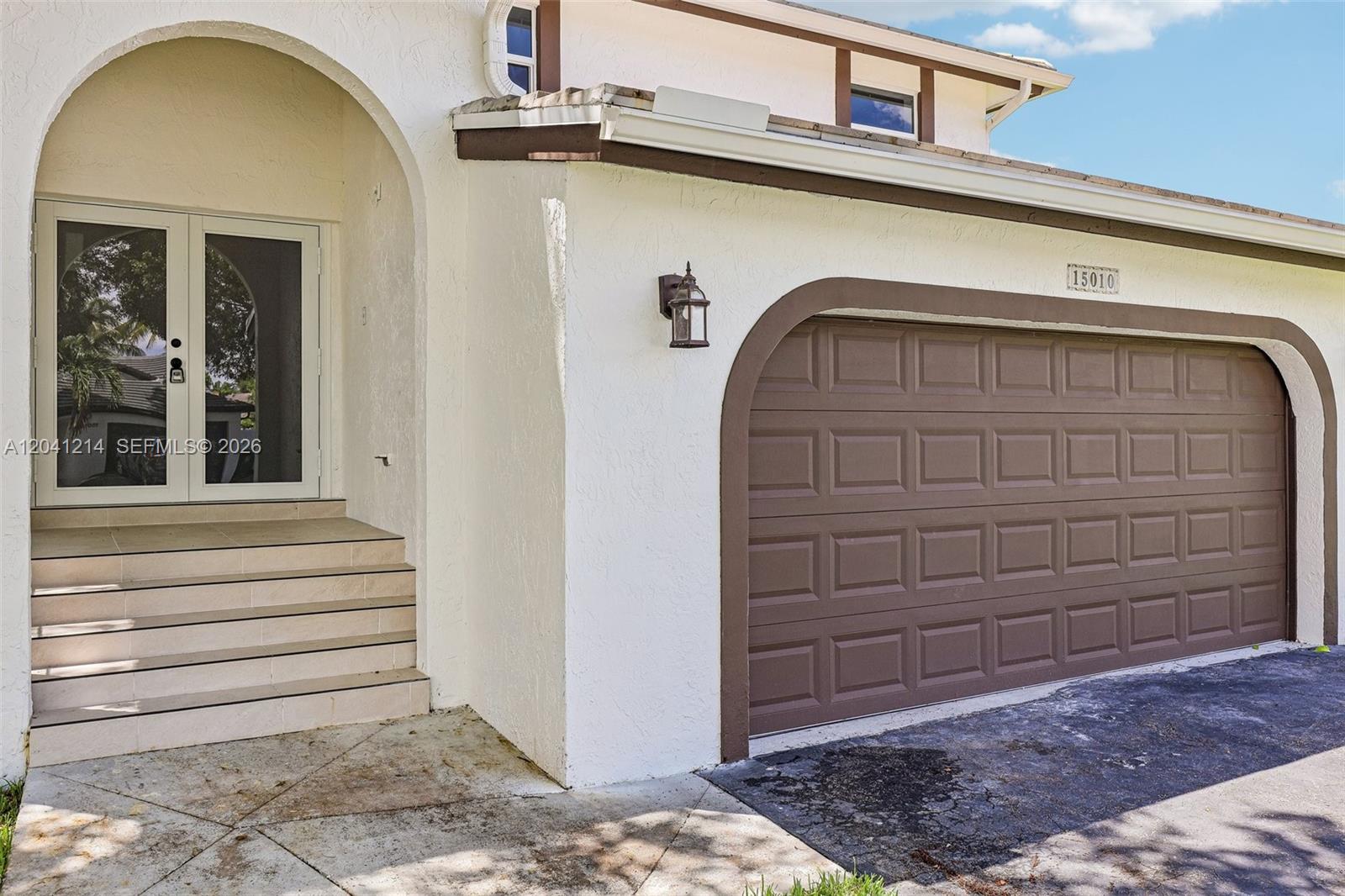The exterior of a house features a brown garage door, arched entryway, and concrete steps — 15010 E Falcons Lea Dr, Davie FL 33331, DAVIE, FL