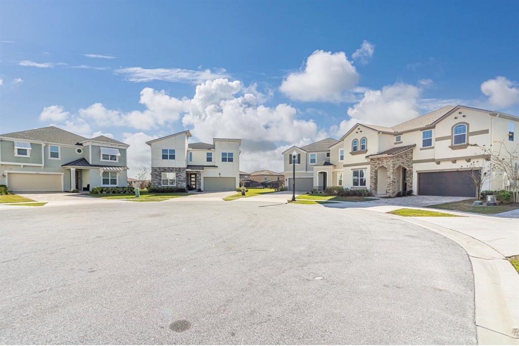 A cul-de-sac features four modern suburban houses with driveways under a blue sky — 8904 CAROLINE BAY COURT, KISSIMMEE, FL