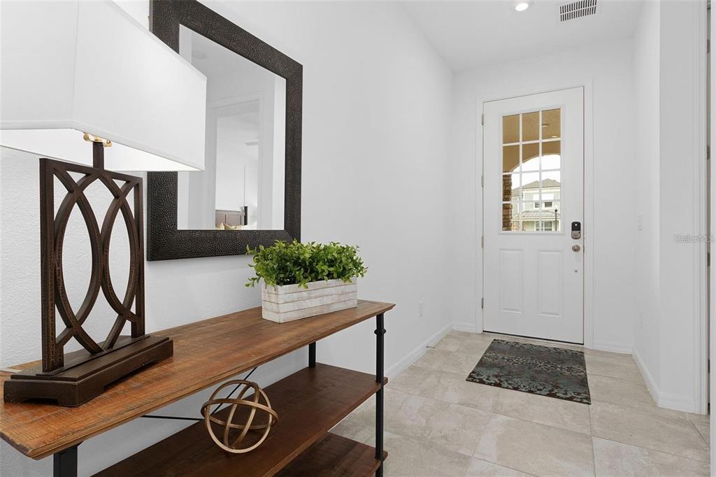 A bright entryway features a wooden console table, a decorative mirror, and a white door — 8904 CAROLINE BAY COURT, KISSIMMEE, FL