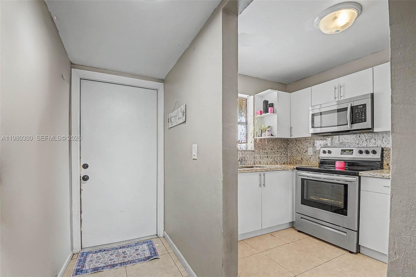 A white door opens into a small kitchen with white cabinets and stainless steel appliances — 6525 W 26th Dr # 37, Hialeah FL 33016, HIALEAH, FL