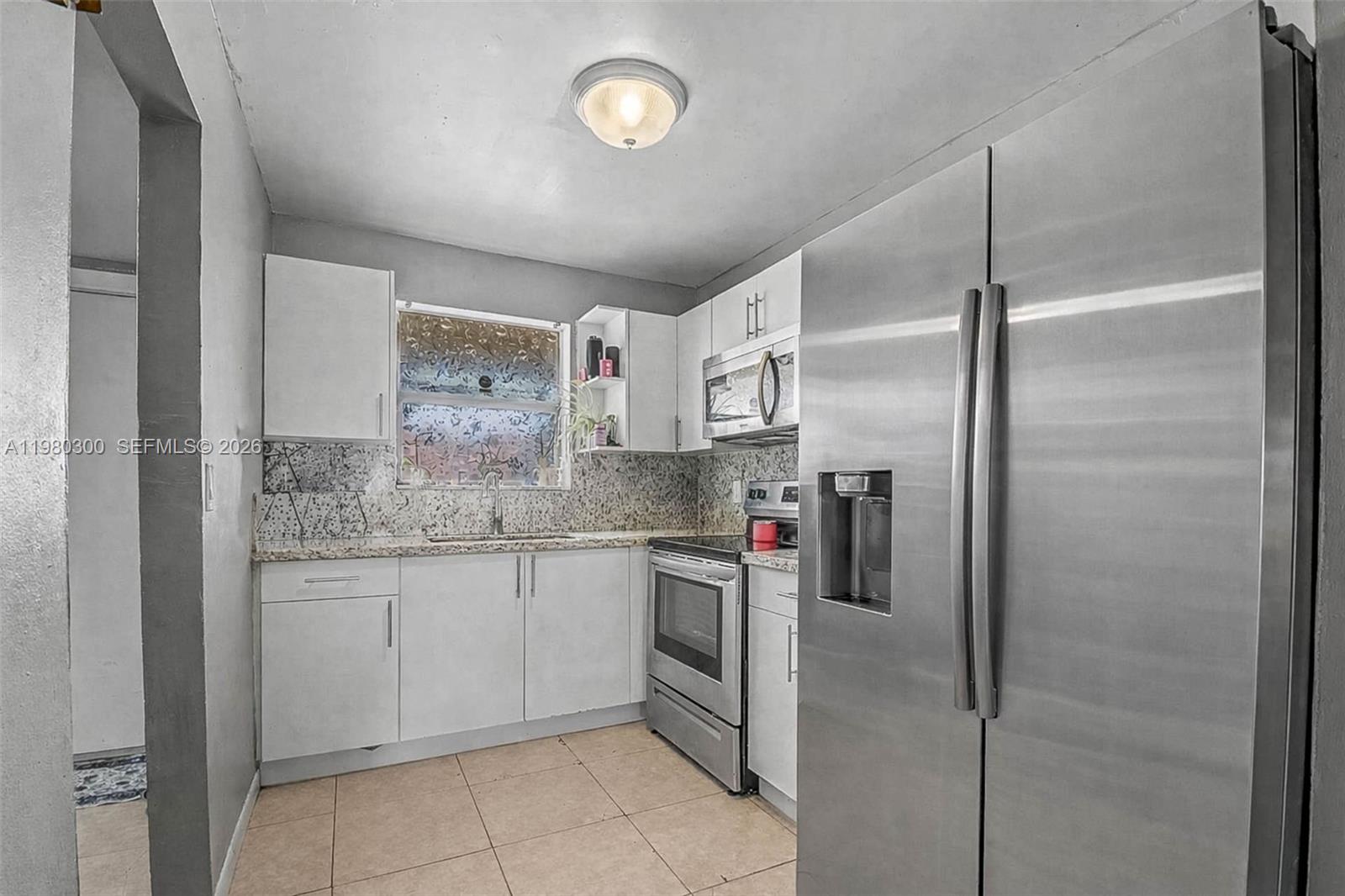 A kitchen features white cabinets, stainless steel appliances, granite countertops, and light-colored tile flooring — 6525 W 26th Dr # 37, Hialeah FL 33016, HIALEAH, FL
