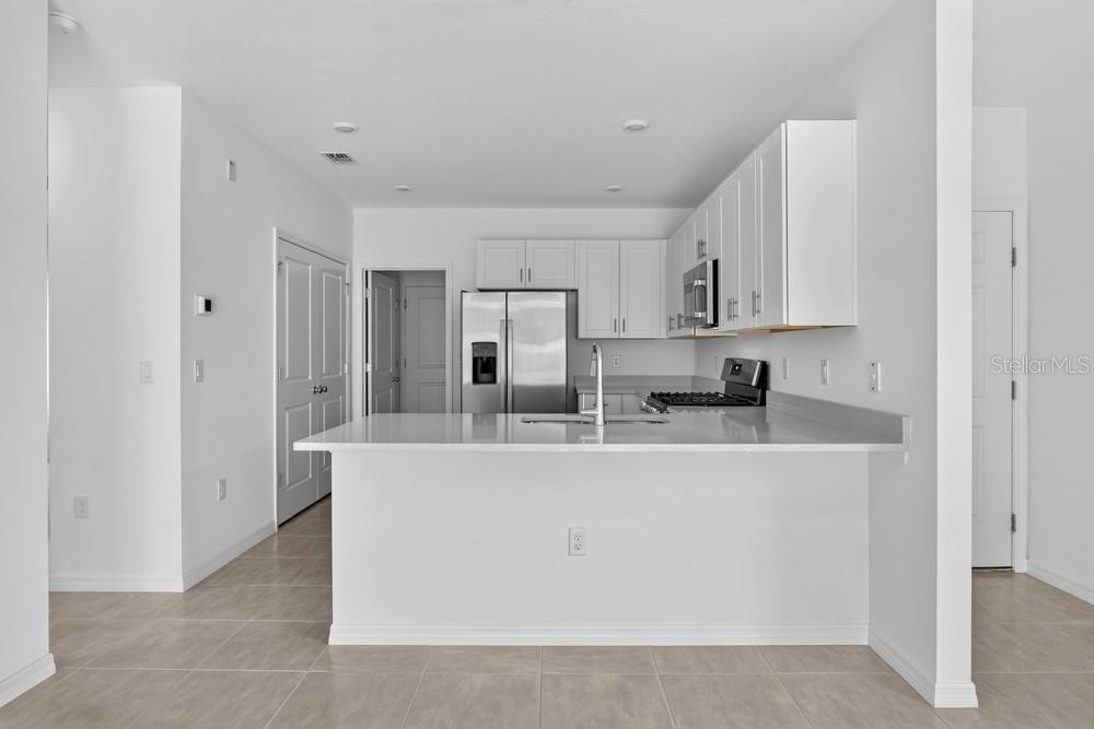 A modern kitchen features white cabinets, stainless steel appliances, and a quartz-topped island — 379 CORNERSTONE DRIVE, GROVELAND, FL