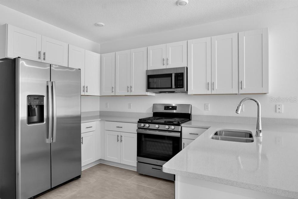 A modern kitchen features white shaker cabinets, stainless steel appliances, and light-colored quartz countertops — 379 CORNERSTONE DRIVE, GROVELAND, FL