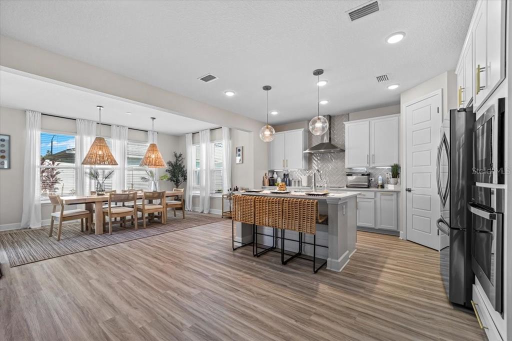 An open-concept kitchen and dining area features light wood flooring, white cabinetry, and woven lighting — 50 MOANA COURT S, PALM COAST, FL