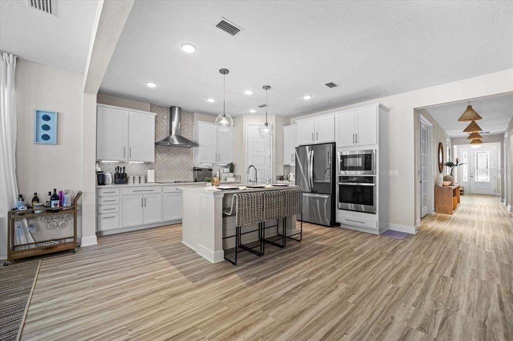 A modern kitchen features white cabinetry, a central island with bar seating, and wood-look flooring — 50 MOANA COURT S, PALM COAST, FL