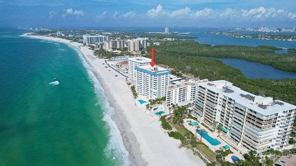 An aerial view shows high-rise beachfront condominiums along a sandy coastline with turquoise water — 1750 BENJAMIN FRANKLIN DRIVE UNIT 9B, SARASOTA, FL