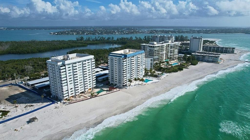 An aerial view shows several high-rise apartment buildings situated directly on a sandy beach — 1750 BENJAMIN FRANKLIN DRIVE UNIT 9B, SARASOTA, FL