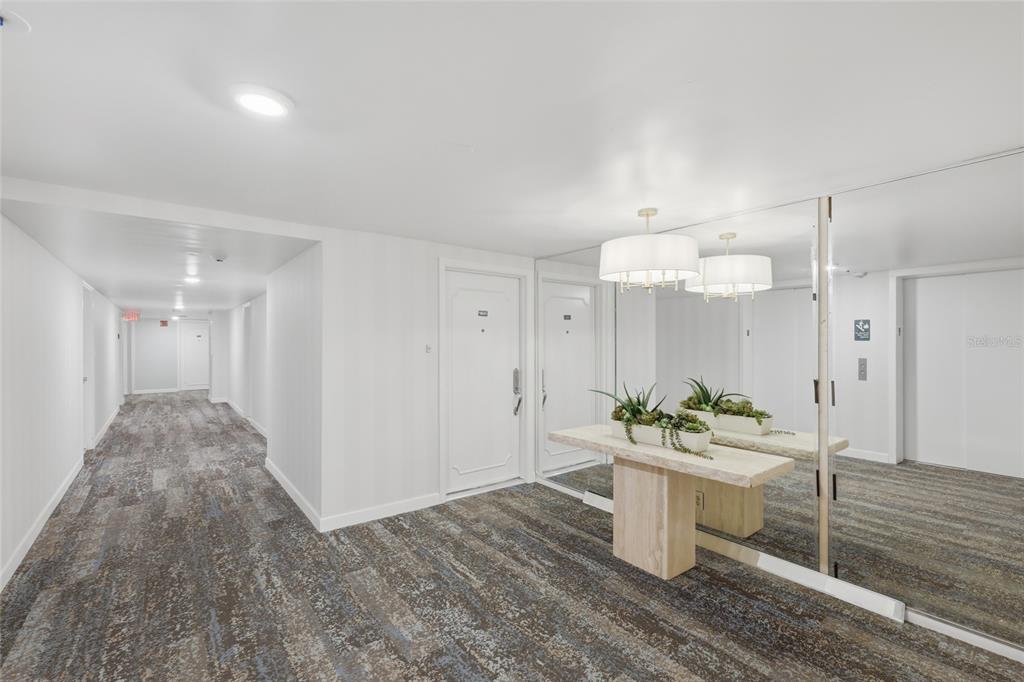 A hallway features patterned carpet, a mirrored wall, and a stone console table with plants — 1750 BENJAMIN FRANKLIN DRIVE UNIT 9B, SARASOTA, FL