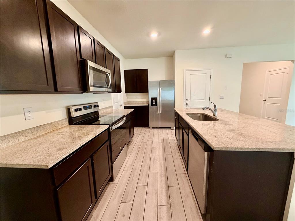 A kitchen features dark wood cabinets, light granite countertops, stainless steel appliances, and tile flooring — 4802 SW 51ST WAY, GAINESVILLE, FL