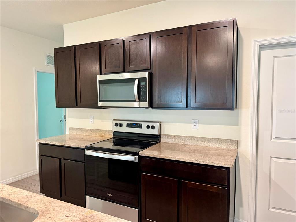 A kitchen features dark wood cabinets, a stainless steel microwave, and a matching electric range — 4802 SW 51ST WAY, GAINESVILLE, FL