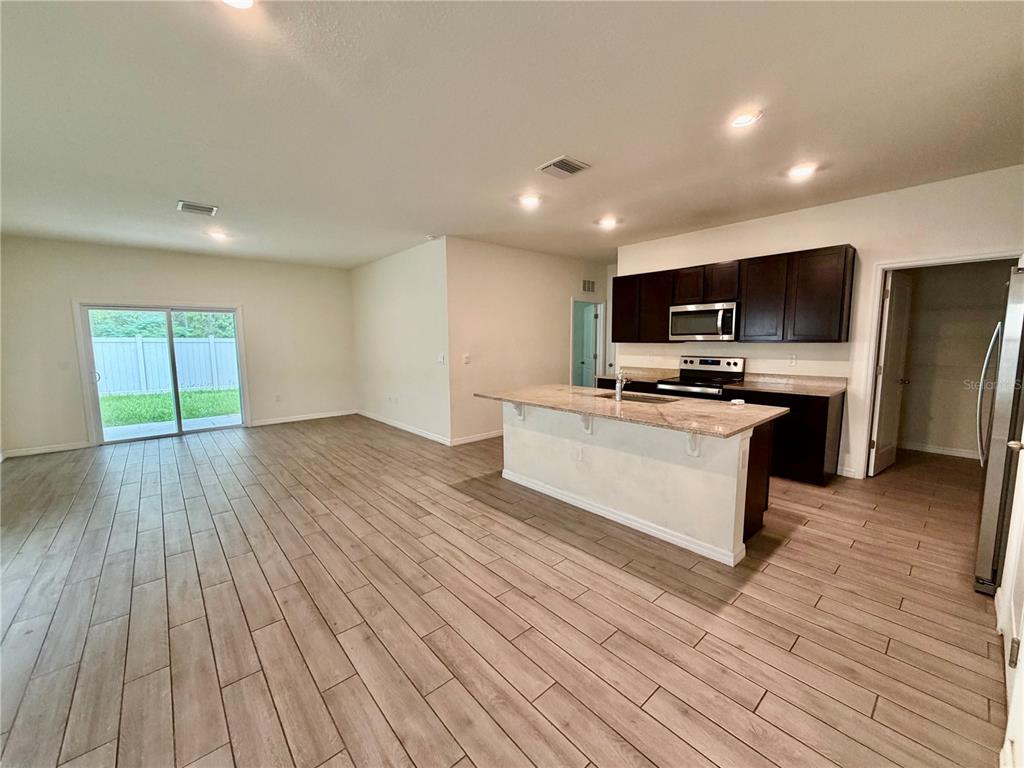 An open-concept kitchen and living area featuring wood-look tile flooring and a granite-topped island — 4802 SW 51ST WAY, GAINESVILLE, FL