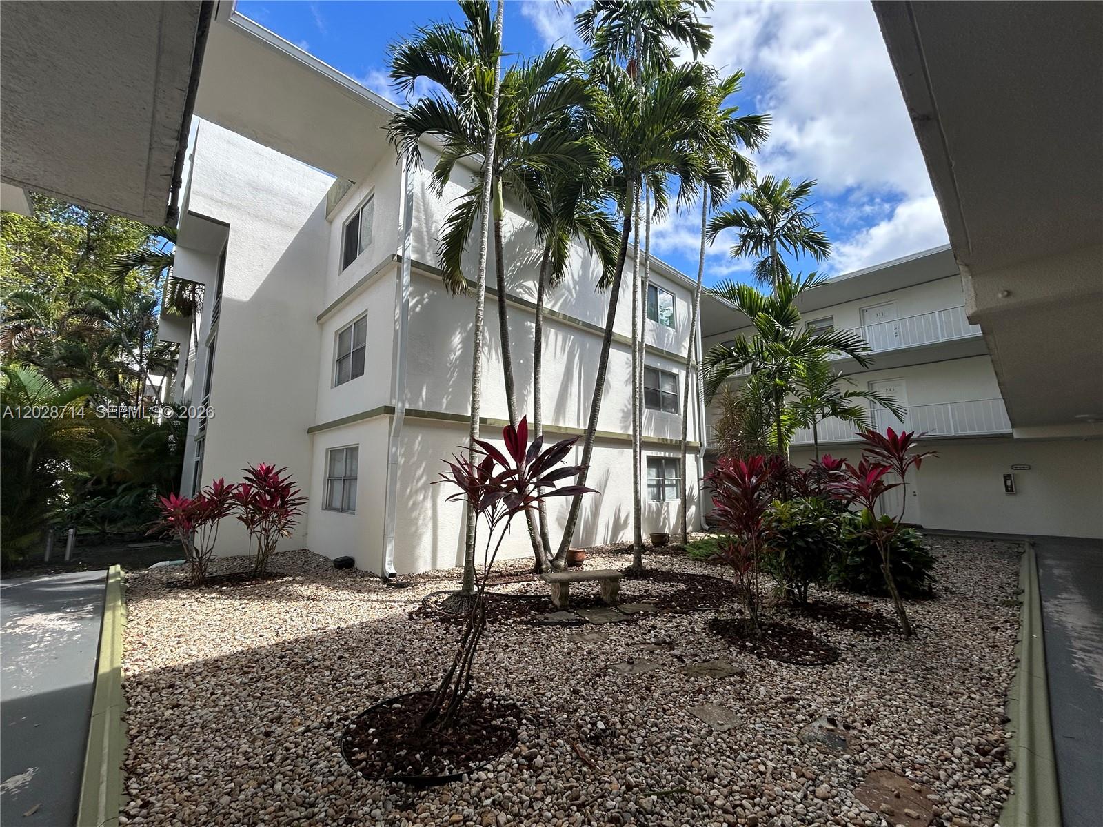 A courtyard with gravel landscaping, tropical plants, and palm trees between two apartment buildings — 4205 N University Dr # 112, Sunrise FL 33351, SUNRISE, FL