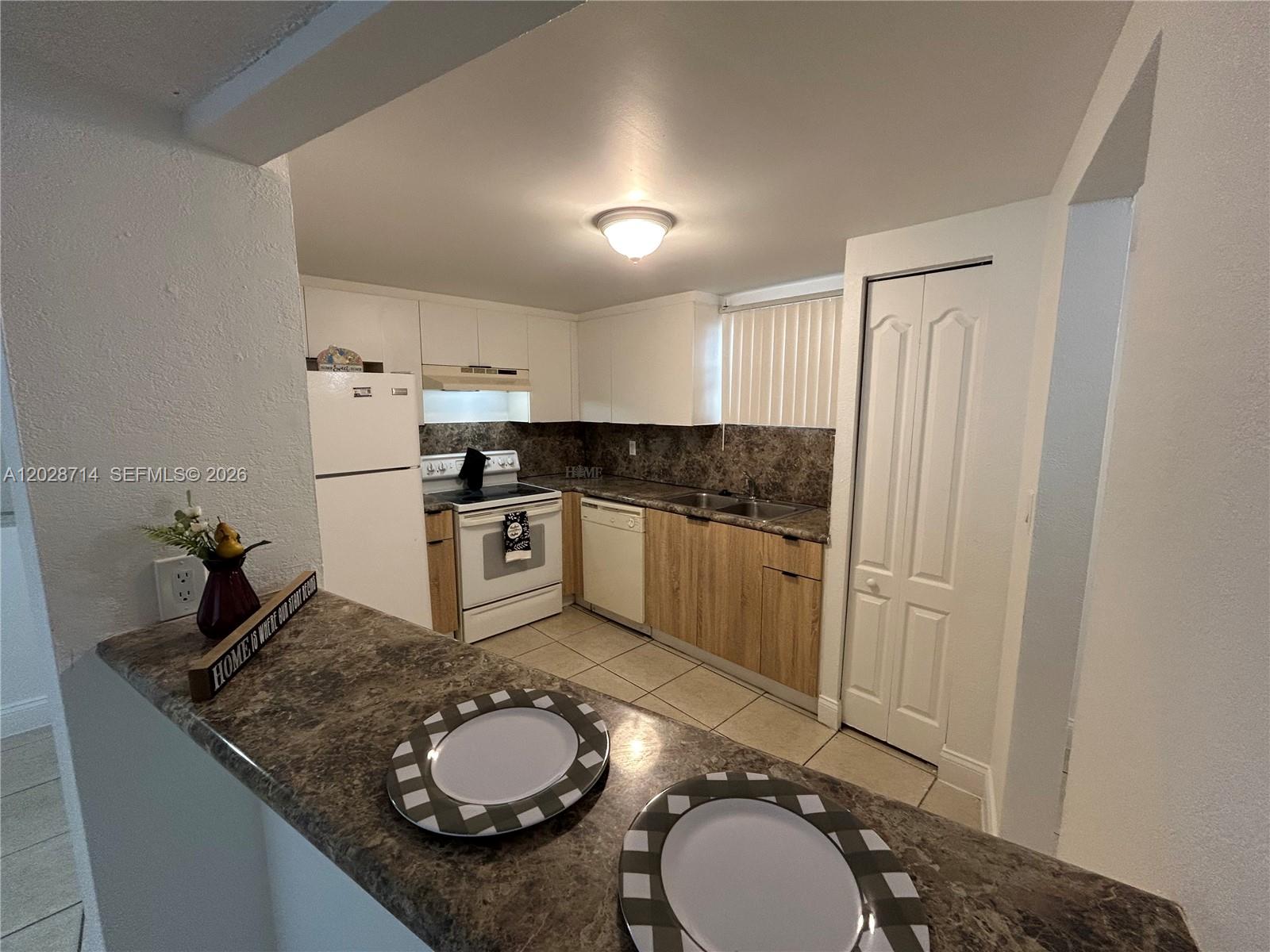 A kitchen features white upper cabinets, wood-look lower cabinets, a white refrigerator, and a breakfast bar — 4205 N University Dr # 112, Sunrise FL 33351, SUNRISE, FL