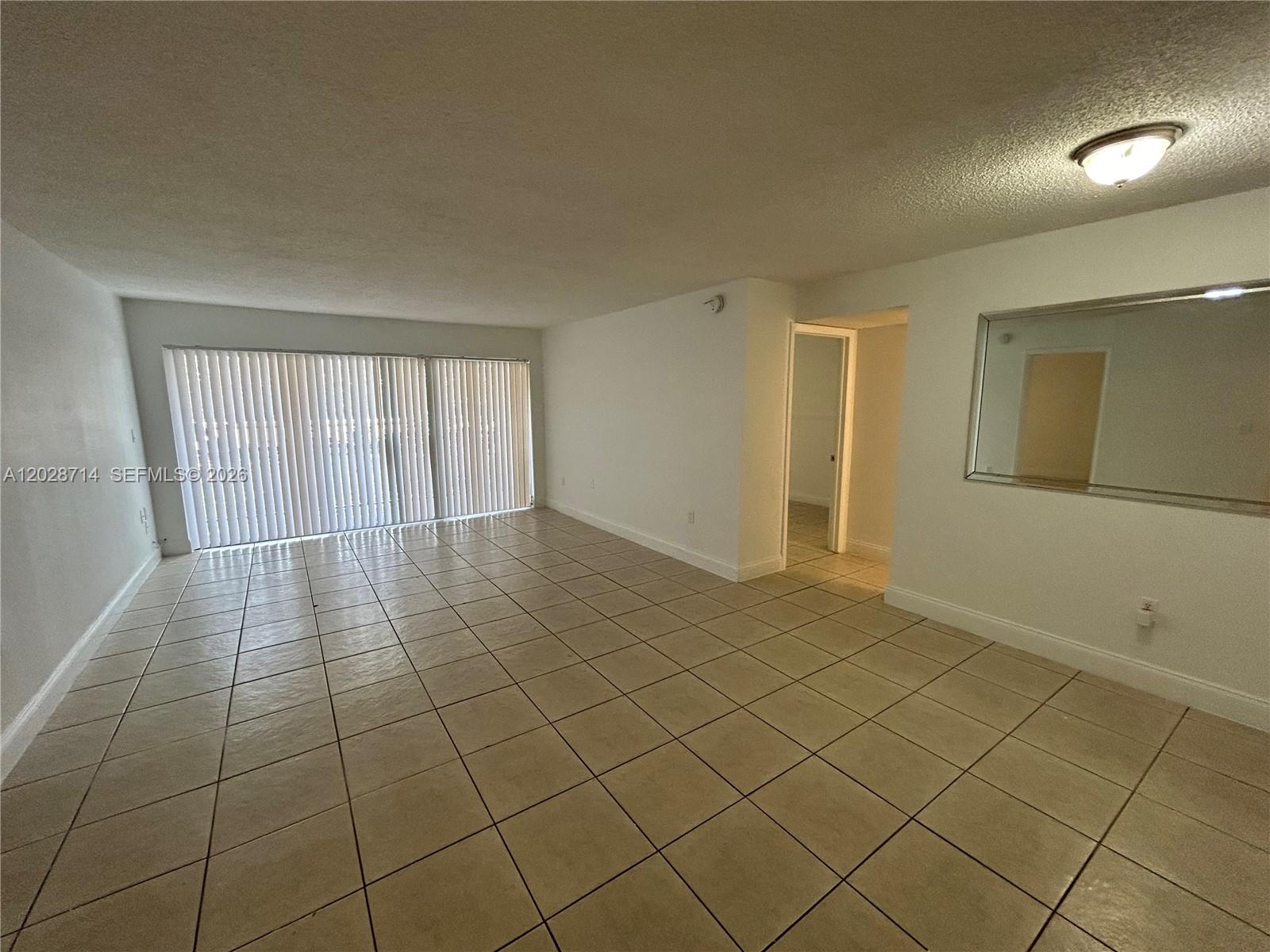 An empty living room features light-colored tile flooring, white walls, and a large sliding glass door — 4205 N University Dr # 112, Sunrise FL 33351, SUNRISE, FL