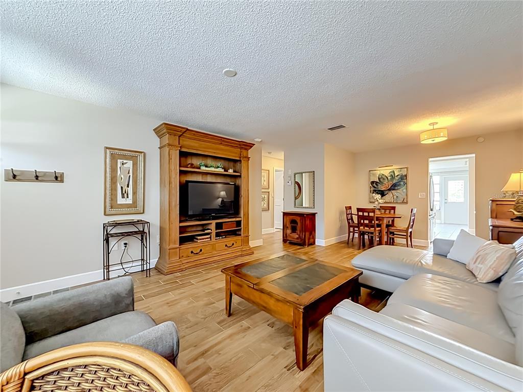 A living room features a large wooden entertainment center, a sectional sofa, and wood-look flooring — 5925 SHORE BOULEVARD S UNIT 107, GULFPORT, FL