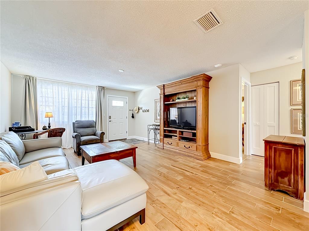 A living room features light wood-look tile flooring, a white sectional sofa, and a wooden entertainment center — 5925 SHORE BOULEVARD S UNIT 107, GULFPORT, FL