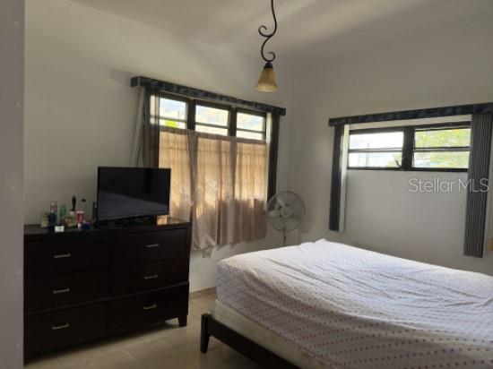A bedroom features a dark wood dresser, a bed with patterned bedding, and two windows — 276 ROSA SANCHEZ, YABUCOA, PR